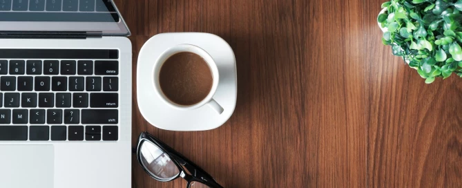Ordinateur portable, café, lunettes et plante sur un bureau en bois pour le télétravail
