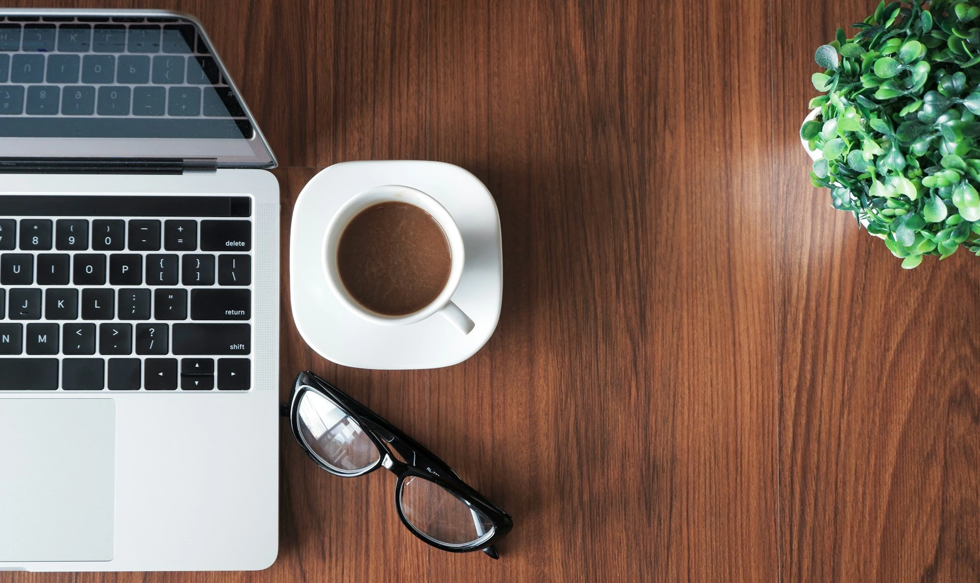 Ordinateur portable, café, lunettes et plante sur un bureau en bois pour le télétravail
